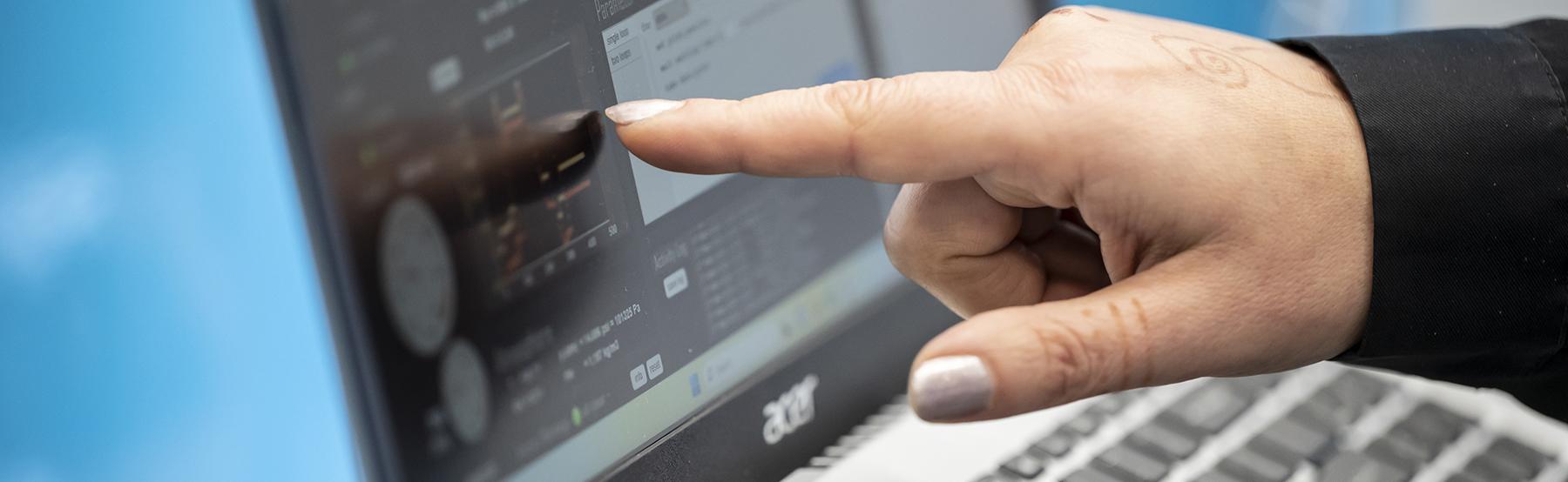 A photo of someone pointing at information on a computer screen.